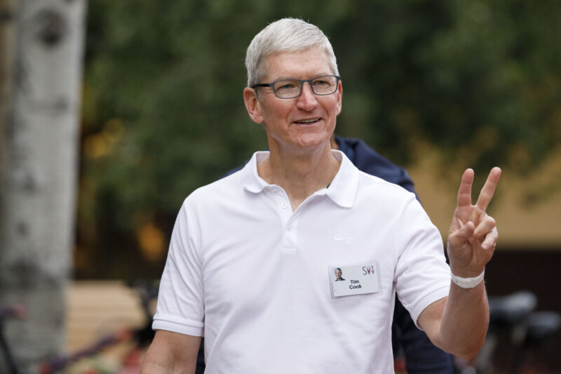 An older man in a white polo shirt flashes a peace sign while walking outdoors.