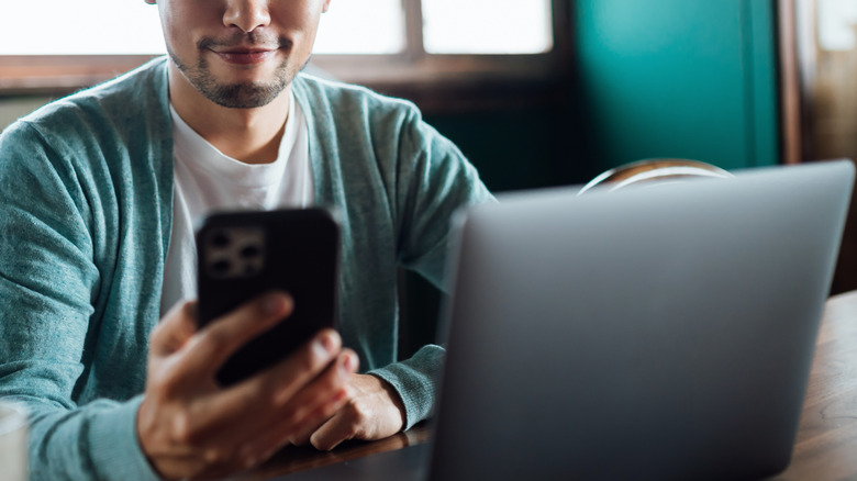 man using iphone and laptop