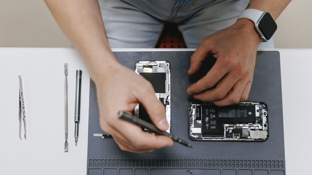 A man uses tolls to work on an iPhoen that has been opened up on a worktable