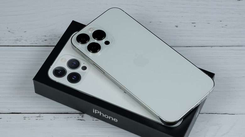 A white iPhone lays atop its box as it sits on a white wooden floor