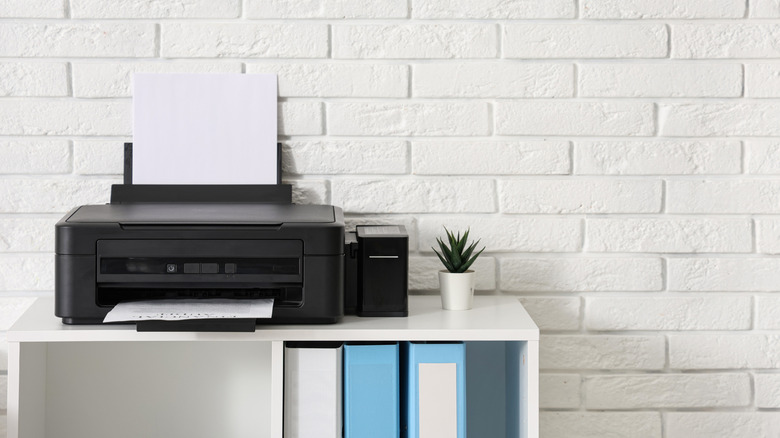 A printer sitting on a shelf in an office in front of a white brick wall.