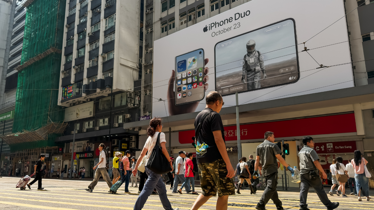 Pedestrians cross a street beneath a large billboard advertising Apple's forthcoming iPhone Duo